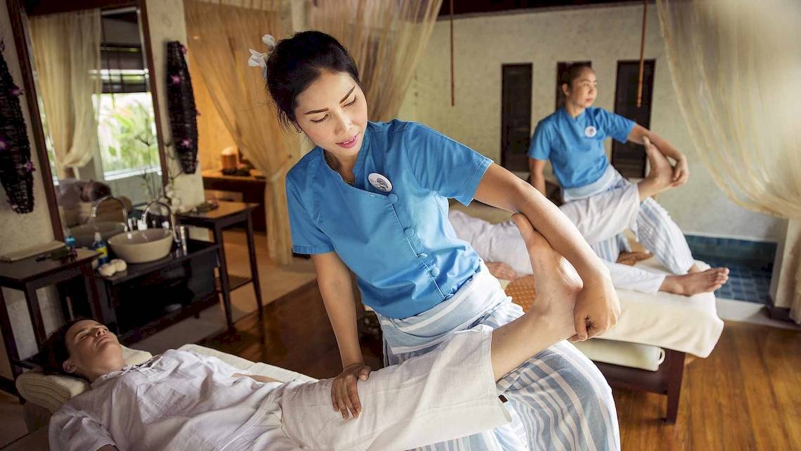 Massage im Robinson Khao Lak Hotel: Eine Frau massiert einen Mann, während eine andere im Hintergrund assistiert.