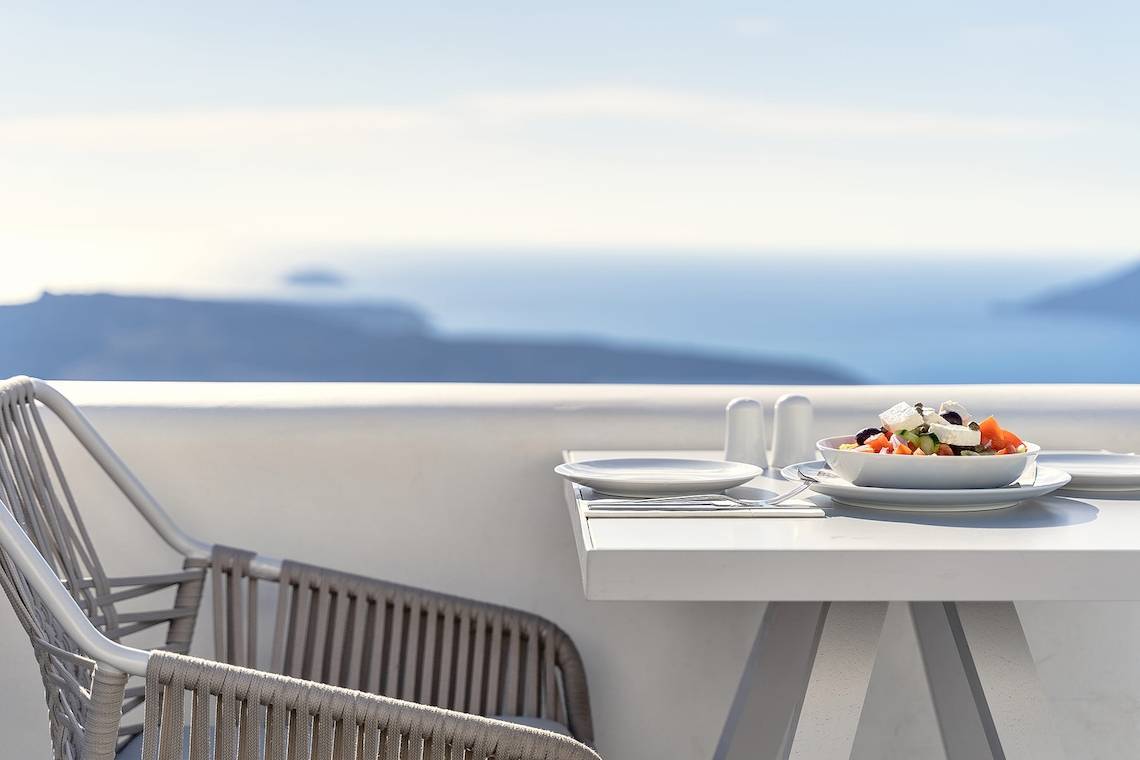 Ein Tisch auf einer Terrasse mit Blick auf das Meer, darauf steht ein Teller mit Salat.