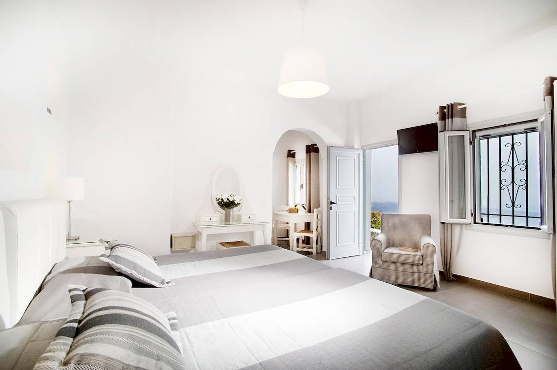 Hotelzimmer von Agali Houses mit weißem Bett, Stühlen, Tisch und Blick auf das Meer.