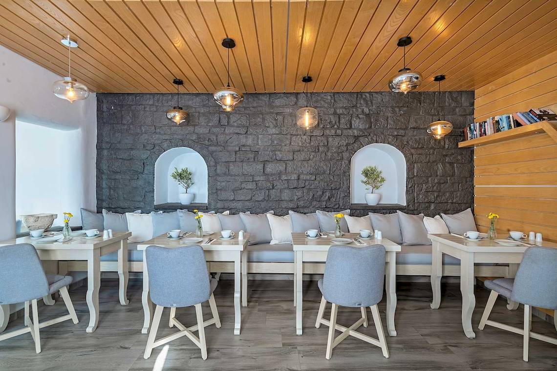 Innenansicht des Restaurants von Agali Houses mit steinerner Wand, Couch, Tischen und Stühlen.