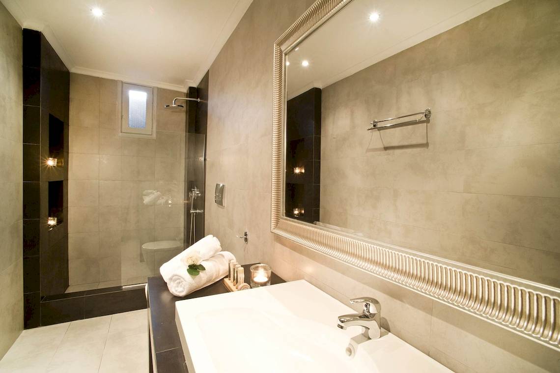 Badezimmer im Agali Houses Hotel mit gefliester Wand, Glasdusche und Badewanne.