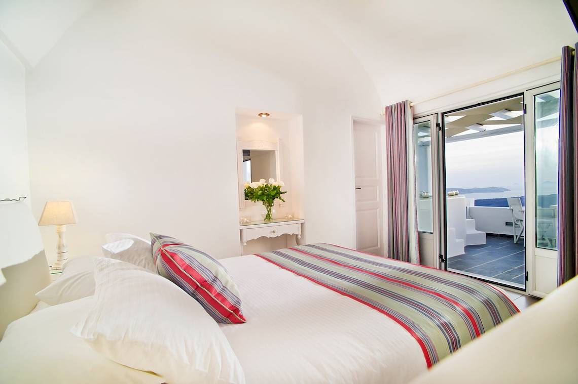 Ein modernes Hotelzimmer mit einem Bett, Kissen, Blumenvase und Meerblick durch eine Glastür.