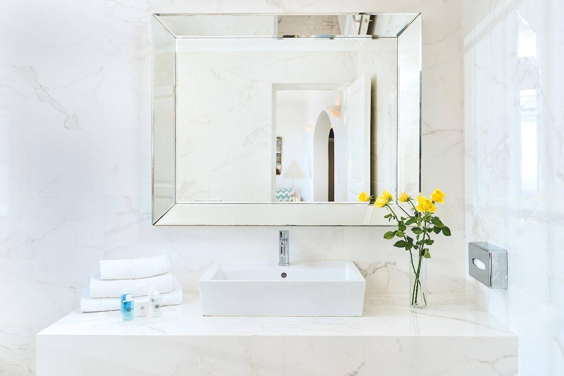 Badezimmer von Agali Houses mit weißem Waschbecken, Spiegel und gelben Rosen in einer Vase.