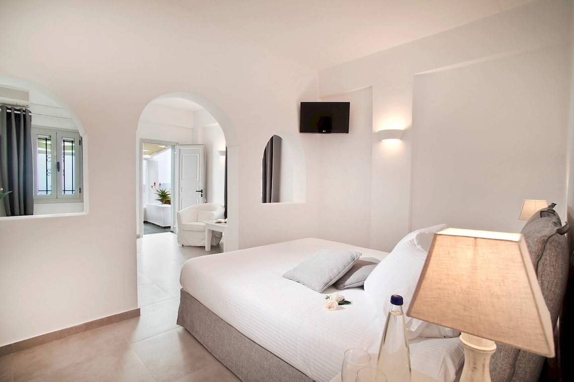 Innenansicht eines Zimmers der Agali Houses mit weißem Bett, Tisch, Lampe und Fernseher.