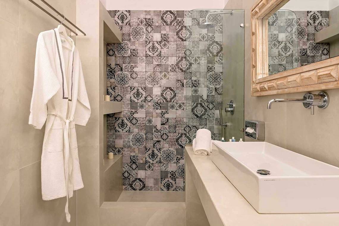 Badezimmer des Agali Houses Hotels mit weißen Fliesen und gemusterten Wandfliesen.