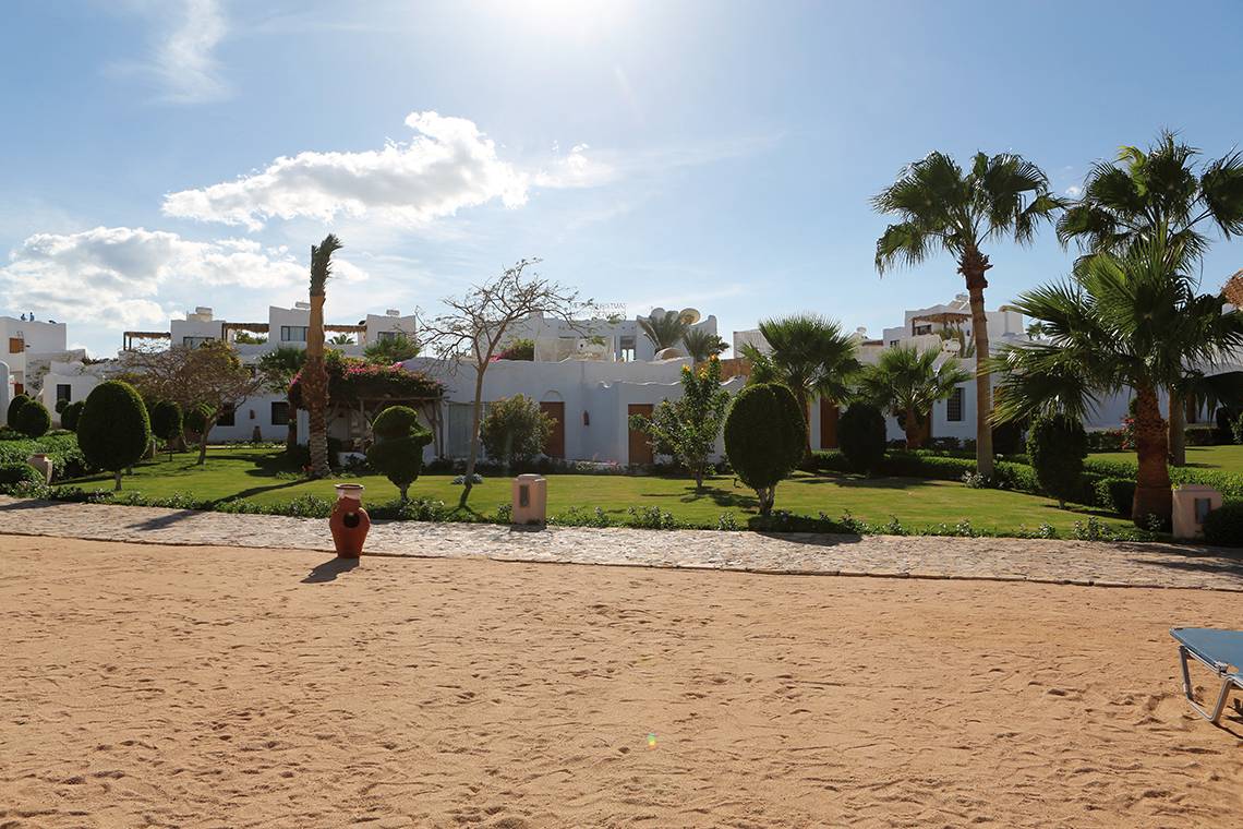 Außenansicht des Sharm Club Beach Resorts mit weißen Gebäuden und üppigem Garten