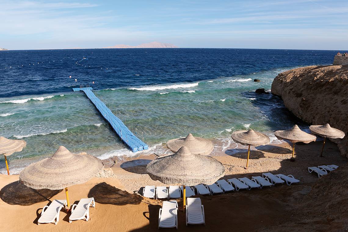 Blick auf den Strand des Sharm Club Beach Resort mit Sonnenschirmen und Liegen.