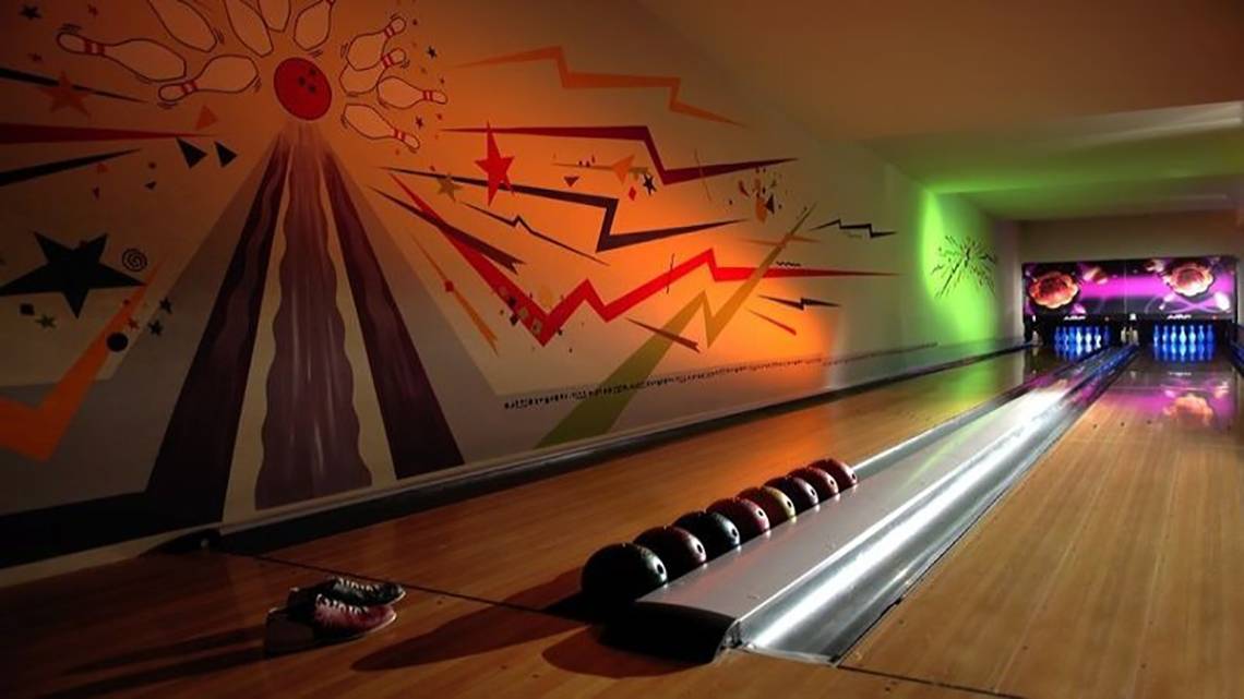 Eine Bowlingbahn im Hotel mit bunten Wandmalereien und Bowlingkugeln in einer Reihe.