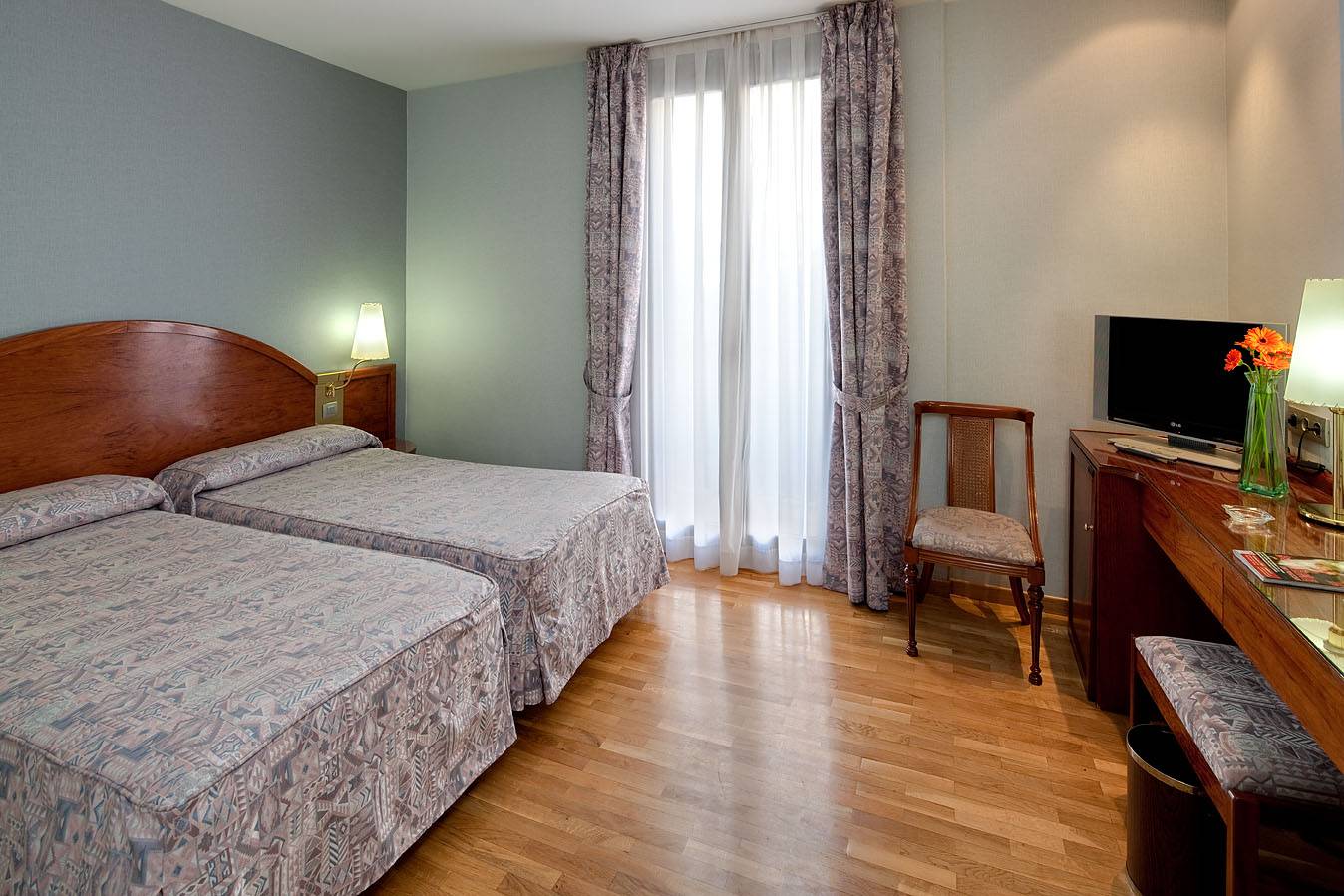 Doppelbett-Zimmer im Gargallo Rialto Hotel mit Fernseher, Schreibtisch, Stühlen und Blumenvase.