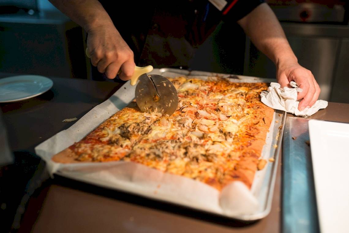 Eine Person schneidet eine Pizza mit einem Pizzaschneider auf einem Tablett im HD Beach Resort.