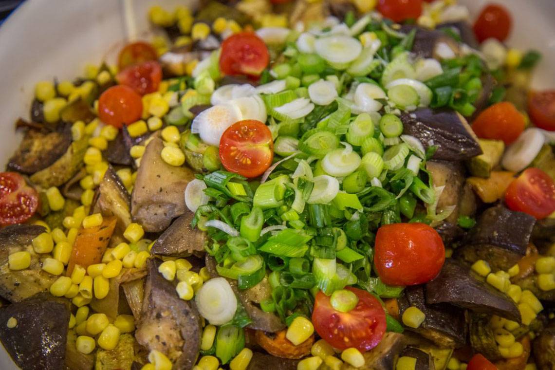 Gewürzter Gemüsesalat mit Mais und Zwiebeln auf einem weißen Teller.