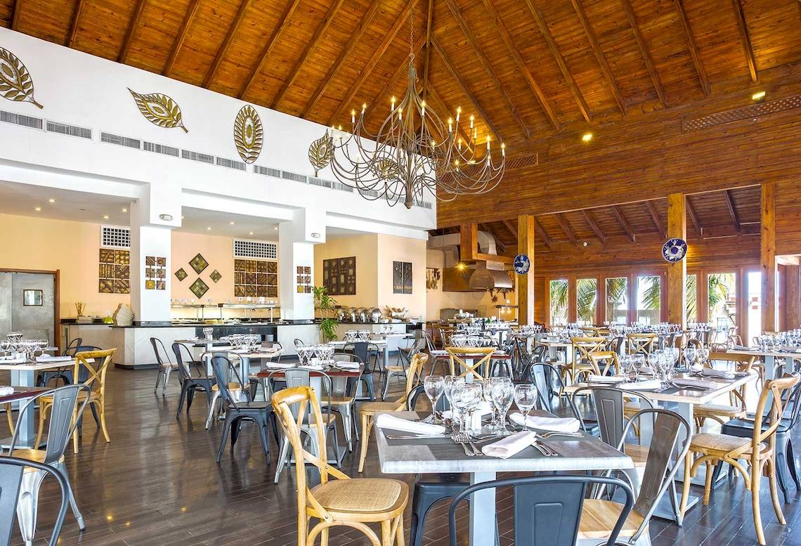 Innenraum eines Hotels mit Holzdecken und einem großen Kronleuchter, gefüllt mit Tischen und Stühlen.