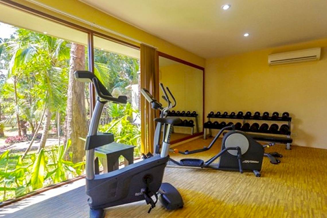 Fitnessraum im Saree Samui Resort mit Geräten und Blick auf Bäume.