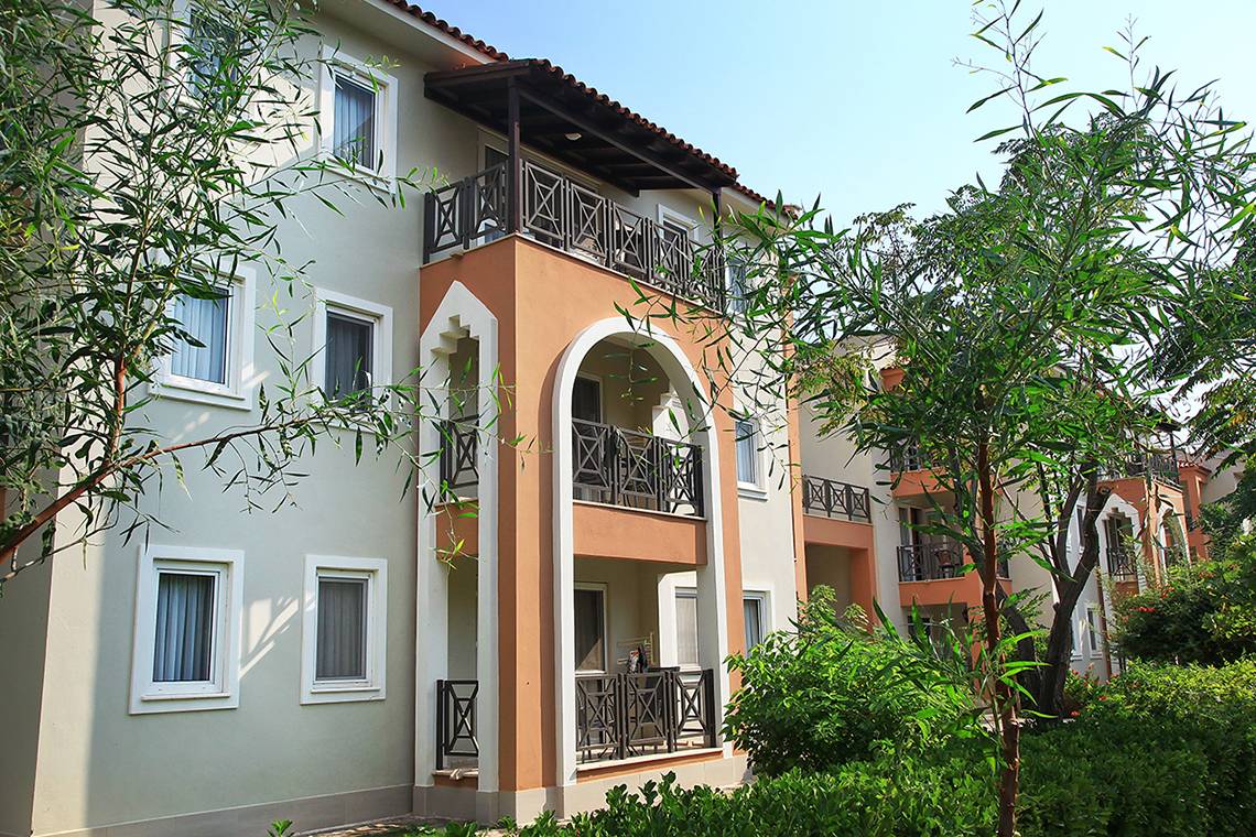 Außenansicht des Club Yali Hotels & Resort mit mehreren Balkonen und umgebenden Bäumen.