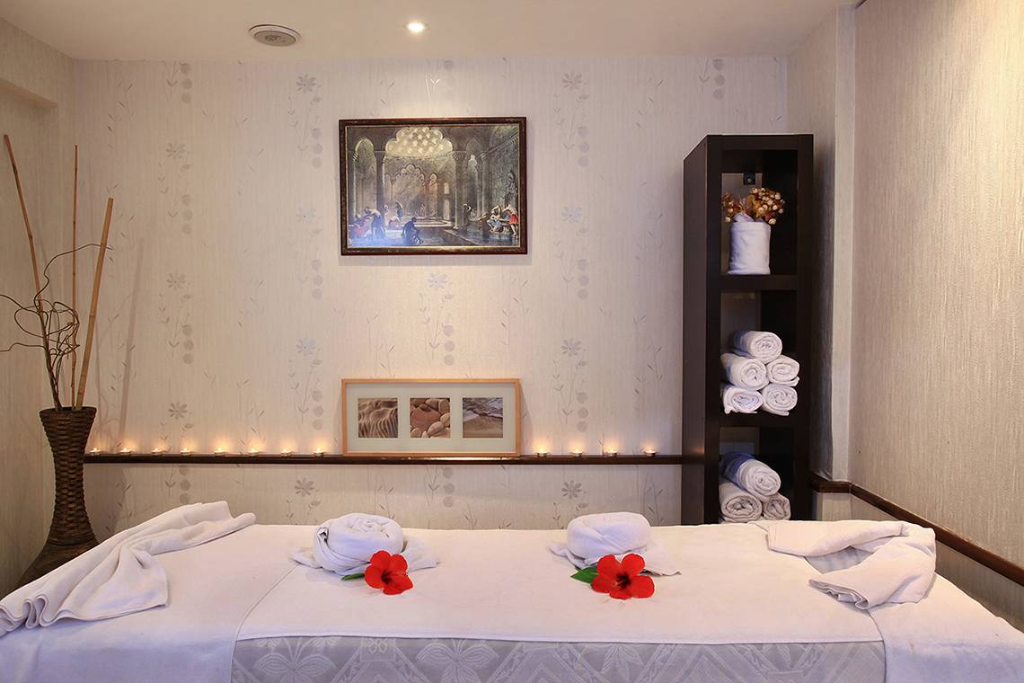 Massage-Behandlungsraum im Club Yali Hotels & Resort mit einem Massagebett, Kerzen und einer Wanddekoration.