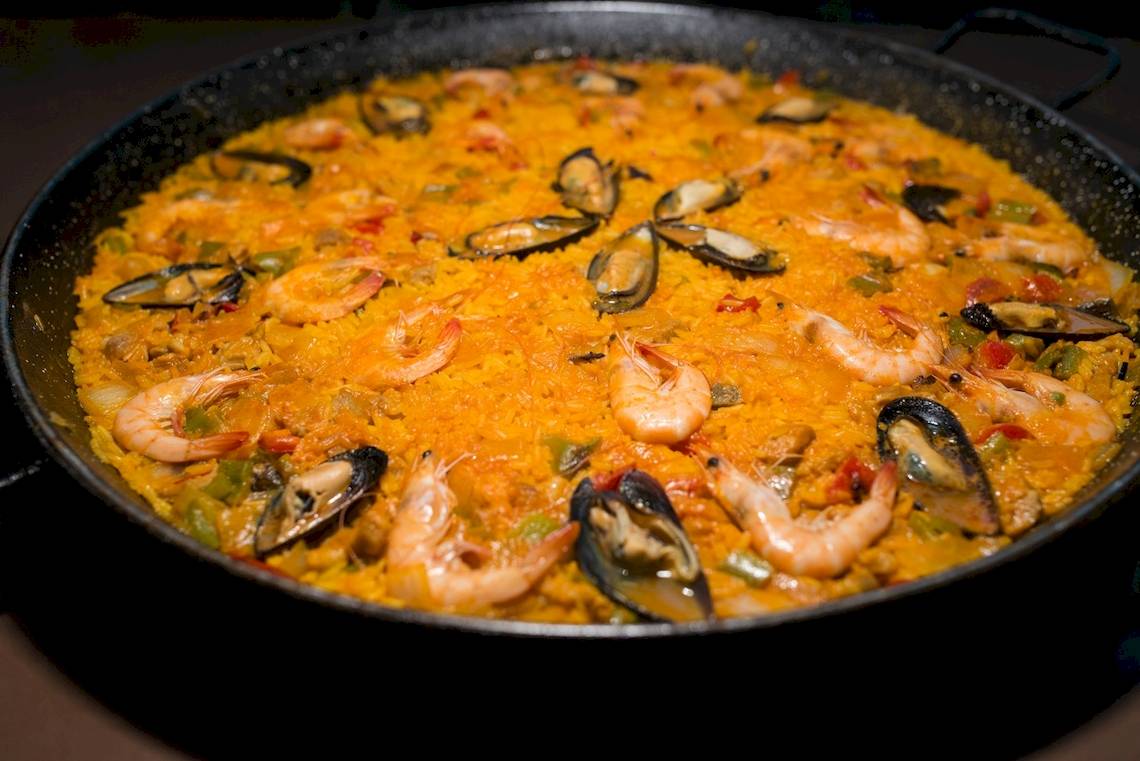 Eine Pfanne mit spanischer Paella, gefüllt mit Garnelen, Muscheln und Reis.