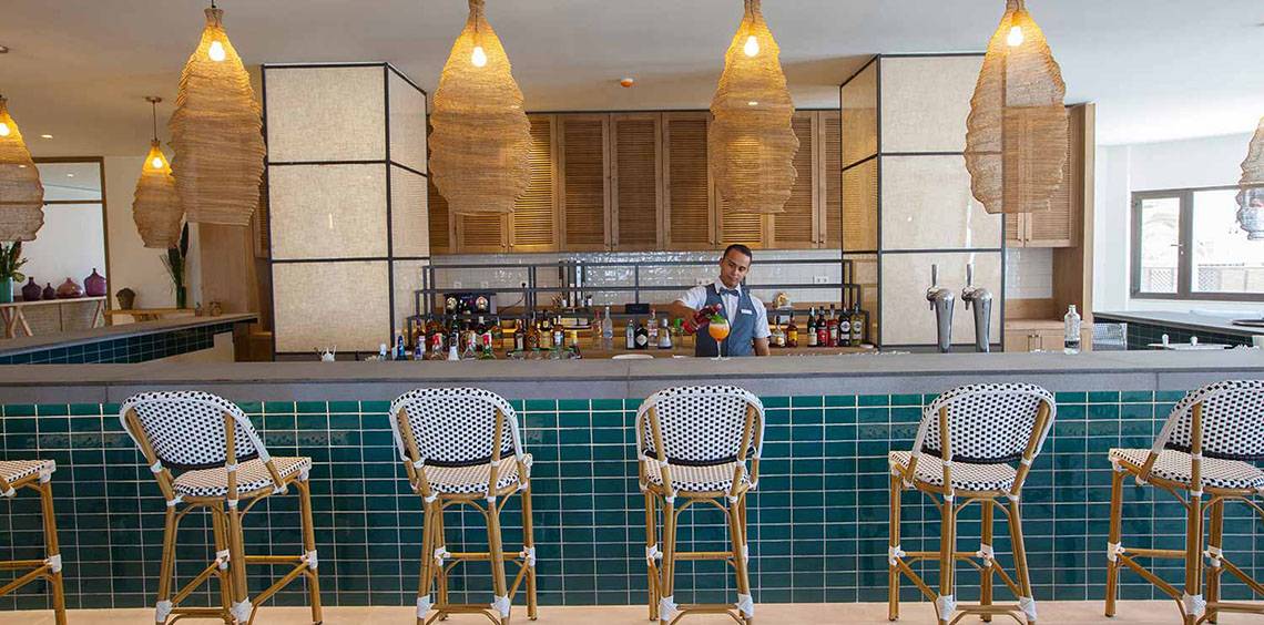 Die Bar im Corallium Dunamar Garden by Lopesan Hotels mit einem Barkeeper, der Getränke zubereitet.