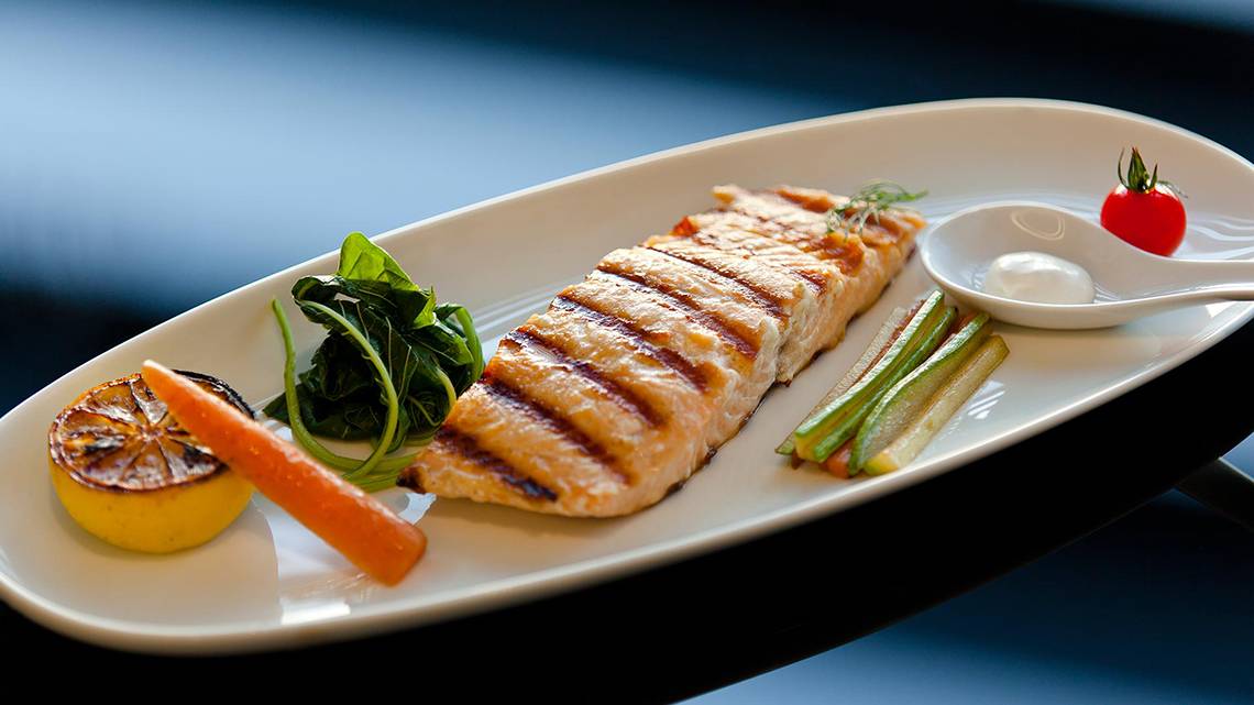 Gegrillter Lachs auf einem weißen Teller mit Spinat, Karotten, Zucchini, Zitrone und Tomatensauce.