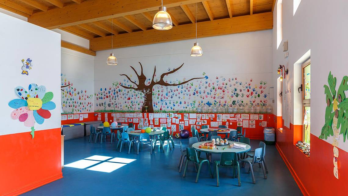 Innenansicht eines Kinderspielzimmers mit bunten Wandgestaltungen, Tischen und Stühlen.