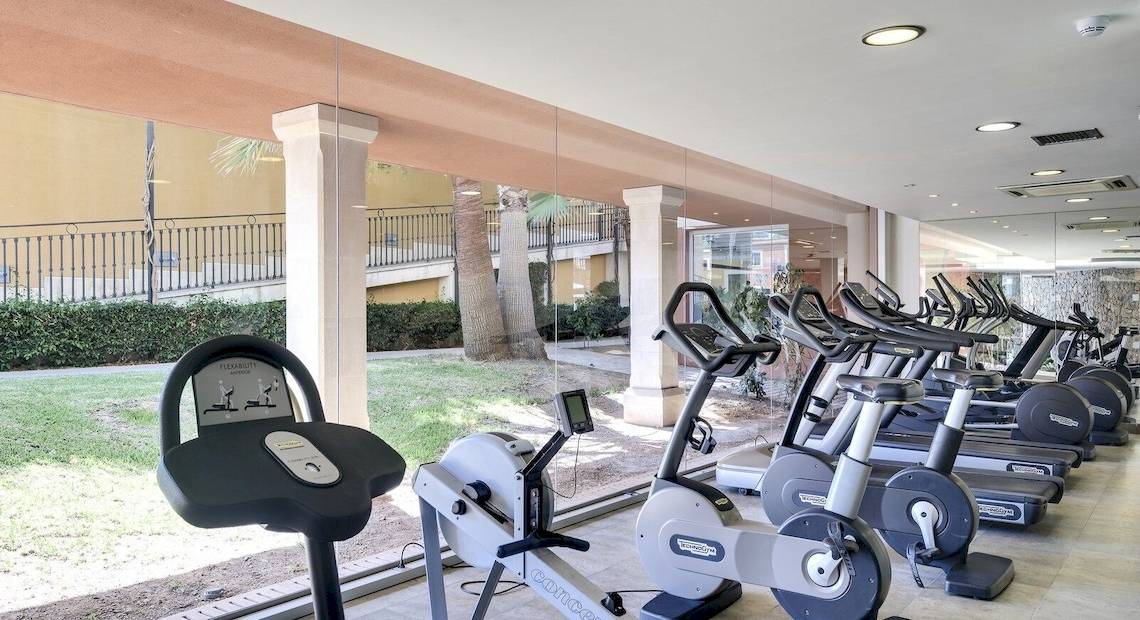 Fitnessstudio im Occidental Playa de Palma Hotel mit vielen Laufbändern und einer grünen Rasenfläche draußen.