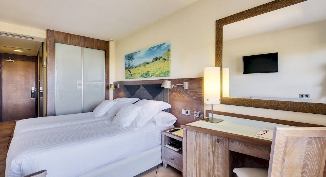 Hotelzimmer im Occidental Playa de Palma mit einem Bett, Schreibtisch, Spiegel und Lampe.