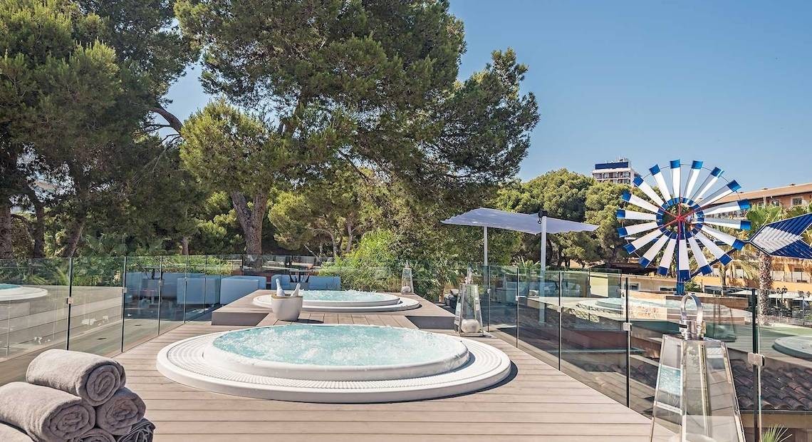 Hotelterrasse mit Whirlpools, einem Schirm und Blick auf Bäume und eine Windmühle