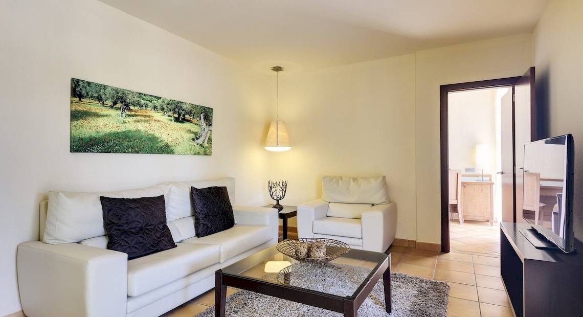 Wohnbereich eines Hotelzimmers mit weißer Couch, schwarzem Tisch und Fernseher.