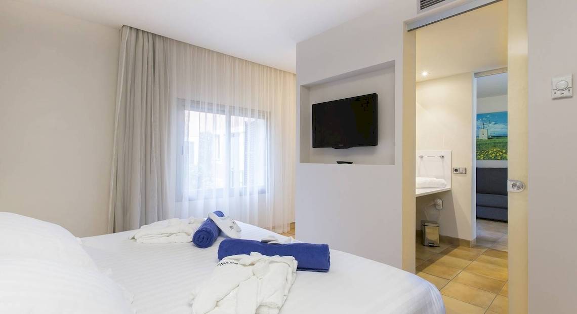 Ein modernes Zimmer im Occidental Playa de Palma mit einem Fernseher an der Wand und einem Bett mit weißen Laken.