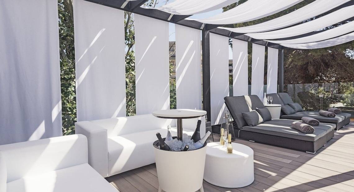 Terrasse des Occidental Playa de Palma mit weißen Lounge-Möbeln, Sonnenliegen und weißen Vorhängen.