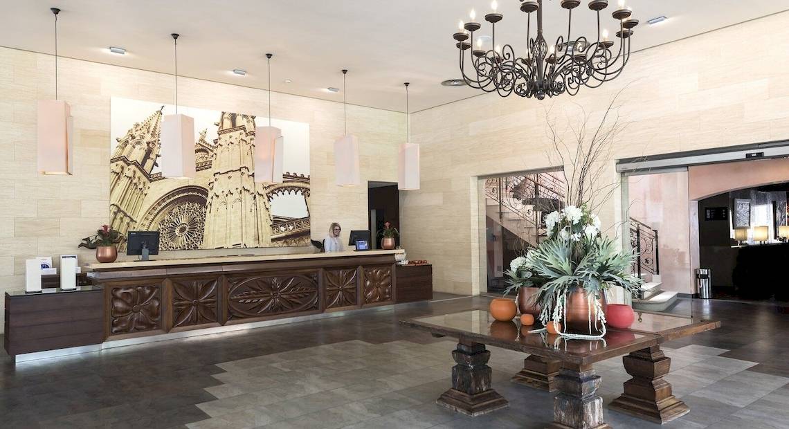 Empfangshalle des Occidental Playa de Palma Hotels mit großem Wandbild, Rezeptionstresen, Sitzgelegenheiten und zentralem Tisch mit Dekoration.