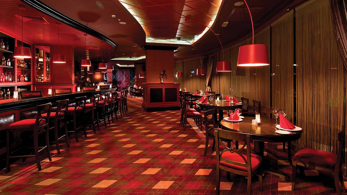 Innenbereich eines Restaurants im Cornelia Diamond Golf Resort & Spa mit roten Stühlen, quadratischem Bodenmuster und hängenden roten Lampen.