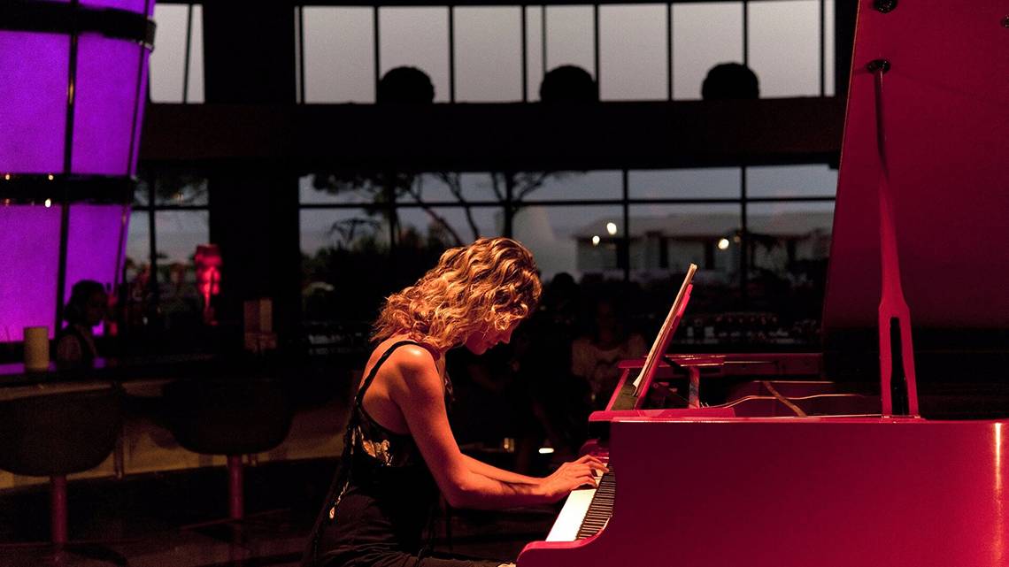 Eine Musikerin spielt ein rotes Klavier im Cornelia Diamond Golf Resort & Spa.