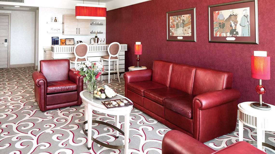 Wohnzimmer im Cornelia Diamond Golf Resort & Spa mit rotem Ledersofa, Esstisch und Dekor.