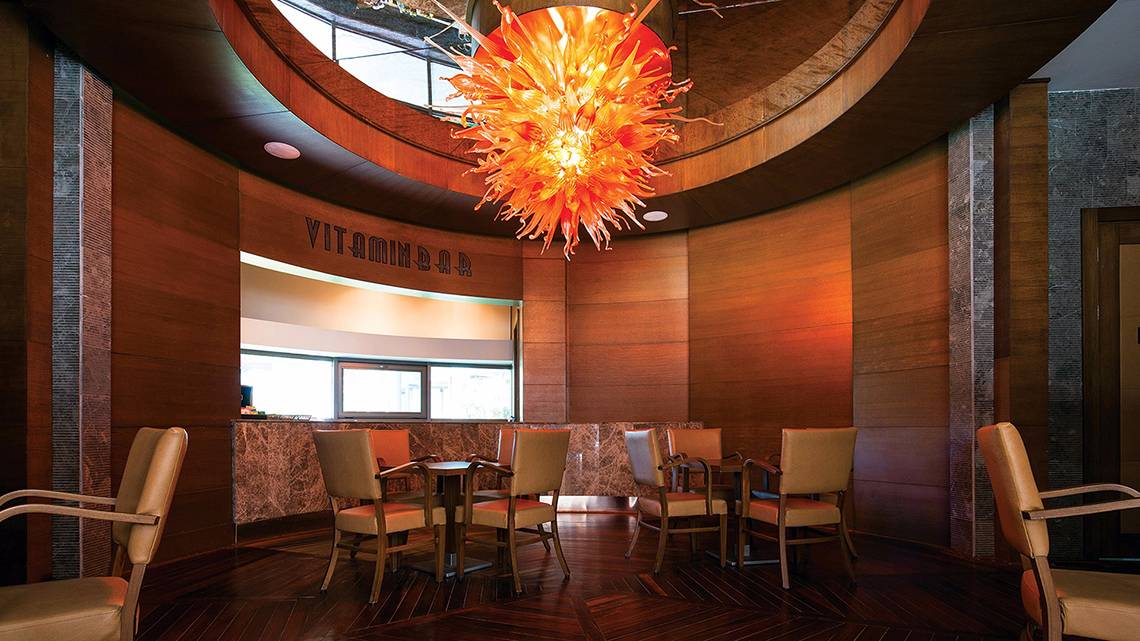 Innenansicht der Vitamin Bar im Cornelia Diamond Golf Resort & Spa mit Holzmöbeln und einer großen Glasleuchte.