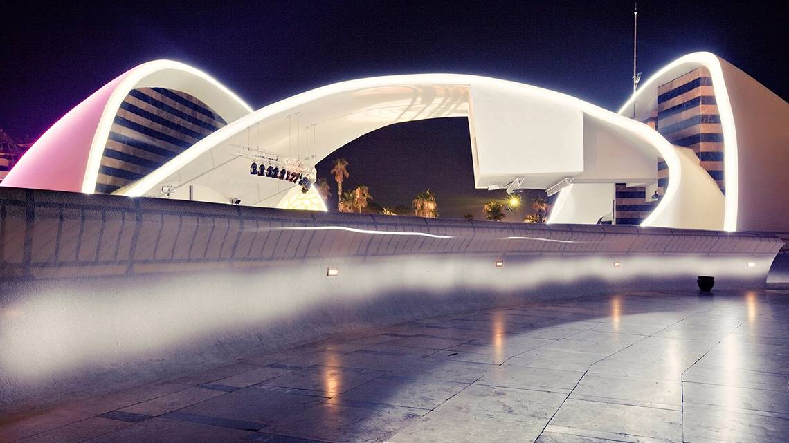Beleuchtete Architektur einer Stadt bei Nacht mit gebogenen Strukturen und reflektierten Lichtern.