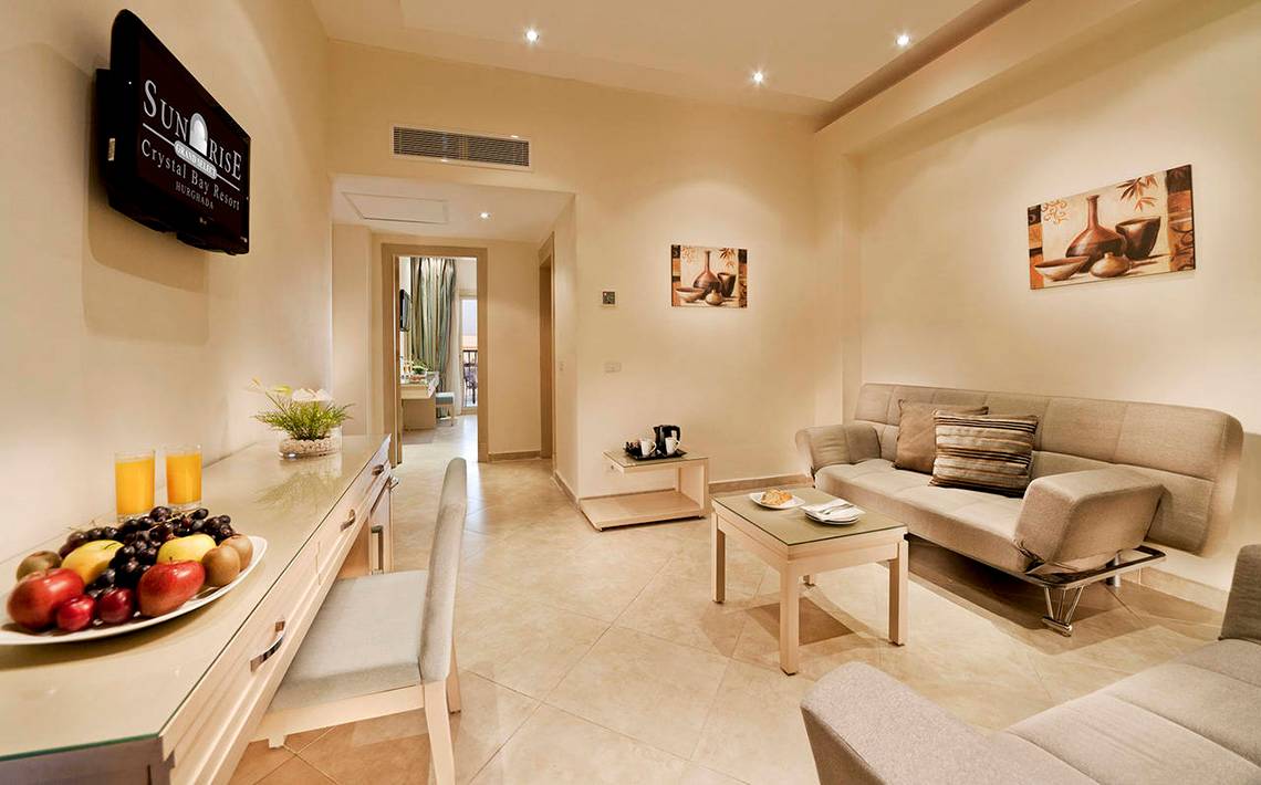 Suite Wohnbereich im Sunrise Crystal Bay Resort mit Fernseher, Sofa, Tisch und Obstteller.