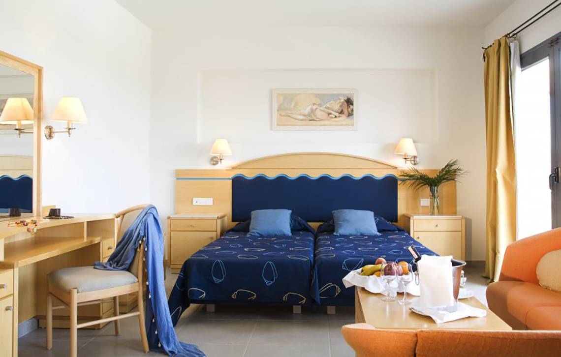 Doppelzimmer im Atlantica Mikri Poli Rhodes Hotel mit zwei Betten, Schreibtisch und Obstkorb auf dem Tisch.