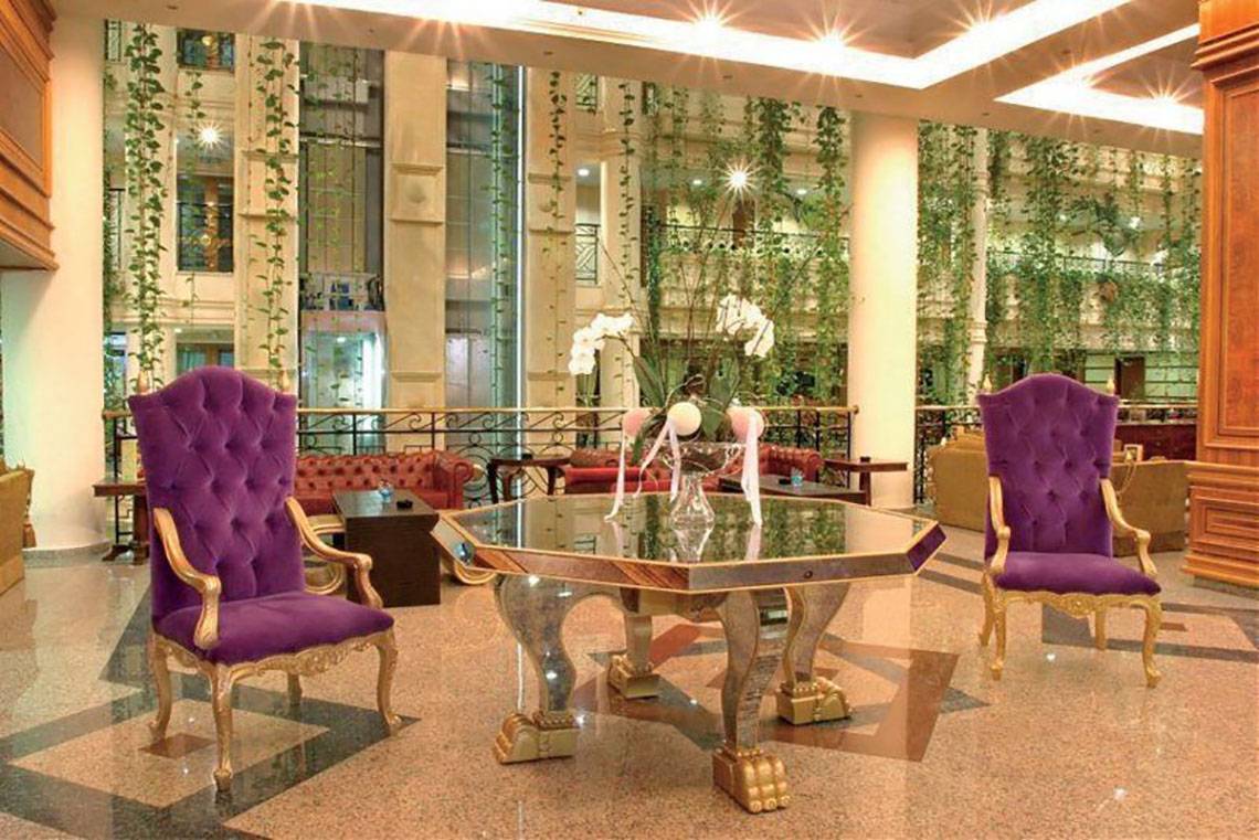 Lobby des Constantinos the Great Beach Hotels mit einem Glastisch und zwei violetten Stühlen.