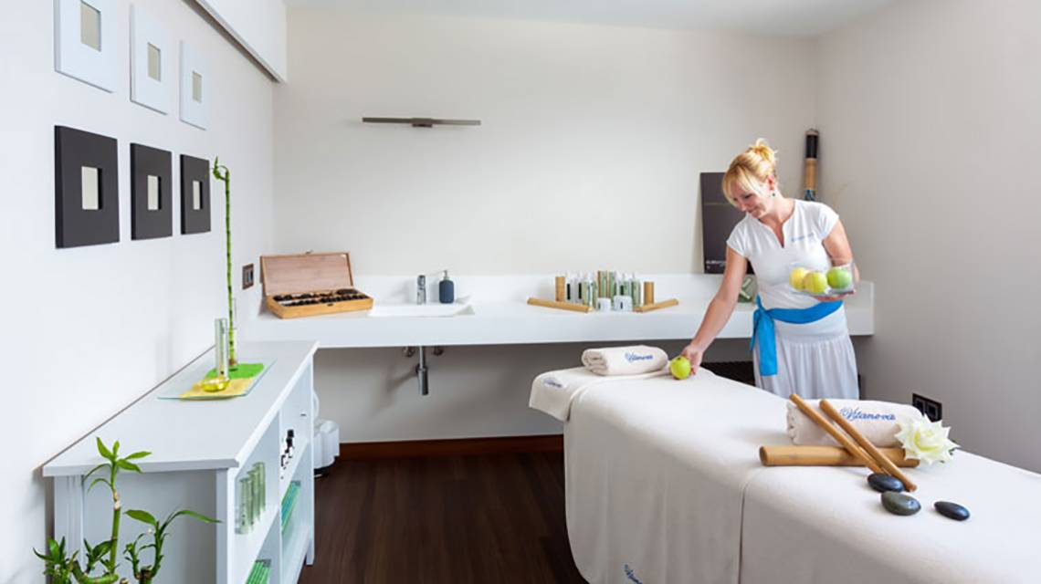 Eine Frau in einem weißen Kleid bereitet einen Massagetisch im Tigotan Lovers & Friends Hotel vor.