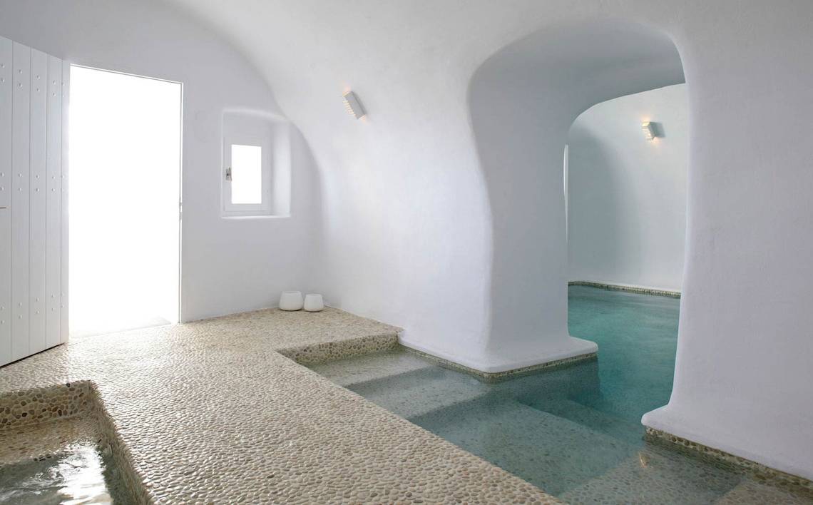 Innenansicht des Badezimmers im Katikies Chromata Hotel auf Santorini mit weißen Wänden und einem kleinen Pool.