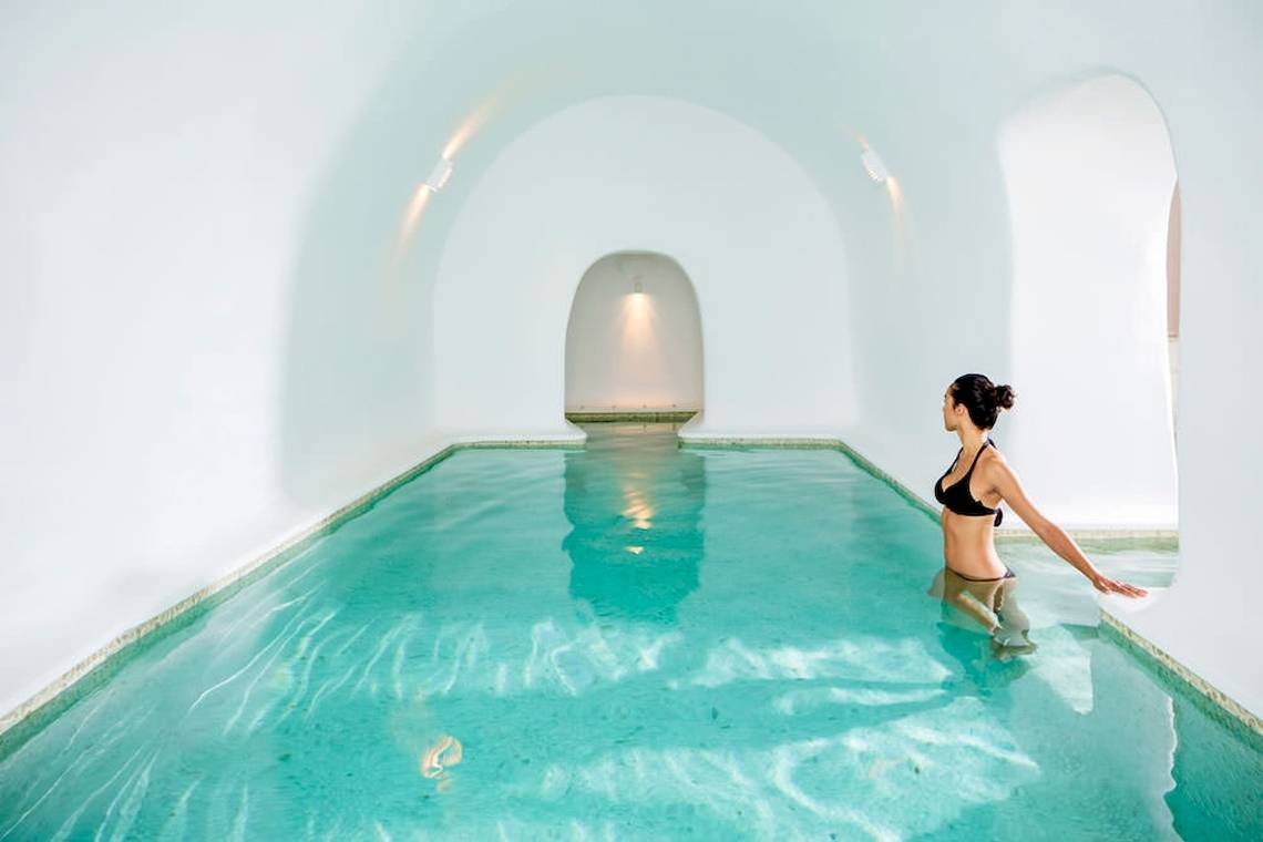 Eine Frau steht in einem weißen Pool von Katikies Chromata Santorini.