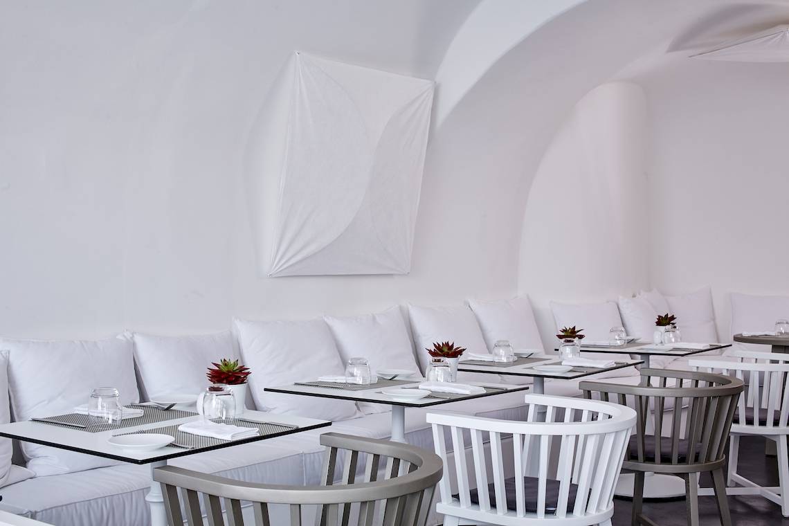 Innenansicht des Katikies Chromata Santorini Restaurants mit weißen Wänden und Möbeln.