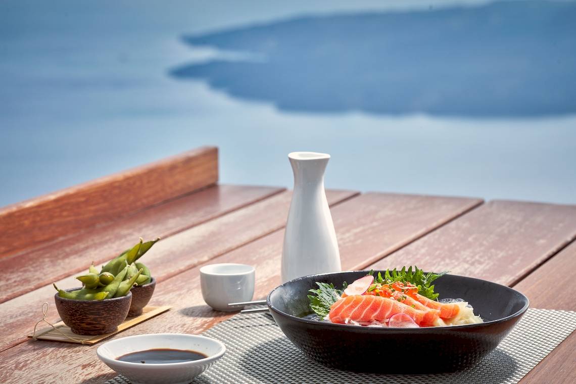 Tisch mit Sushi und Getränken im Freien mit Blick auf das Meer.