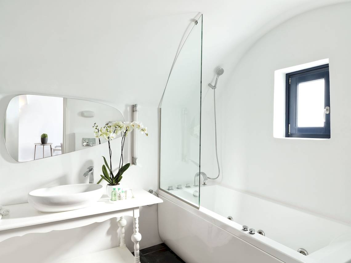Ein Badezimmer im Katikies Chromata Santorini Hotel mit einer weißen Wanne, einem Waschbecken und einem Spiegel.
