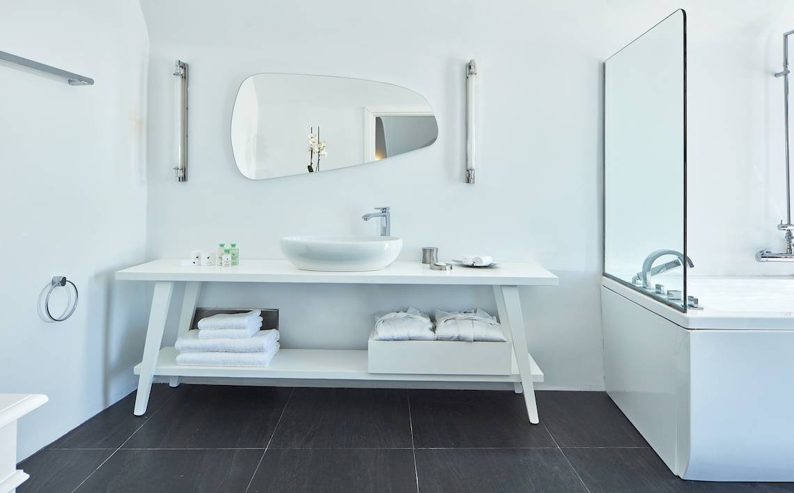 Badezimmer im Katikies Chromata Santorini Hotel mit weißem Waschtisch und Dusche.