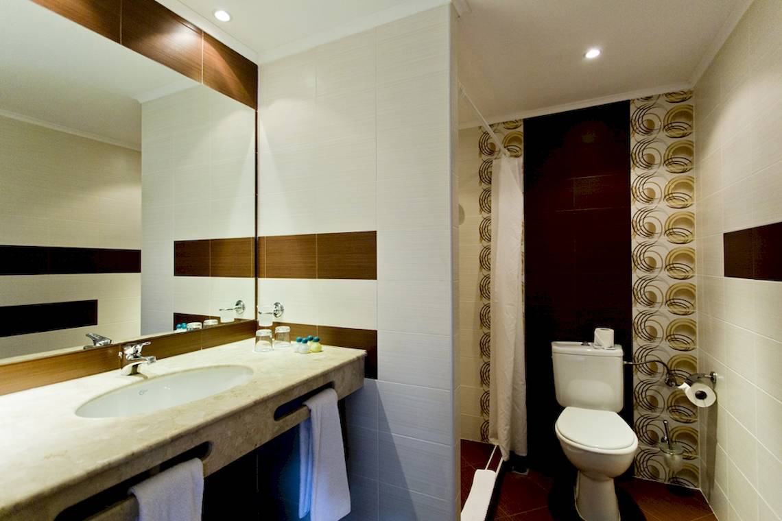 Badezimmer im DIT Evrika Beach Club Hotel mit Waschbecken, Spiegel und Toilette.