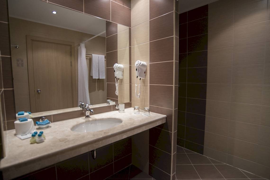 Badezimmer im DIT Evrika Beach Club Hotel mit Waschbecken, Spiegel und Handtüchern.