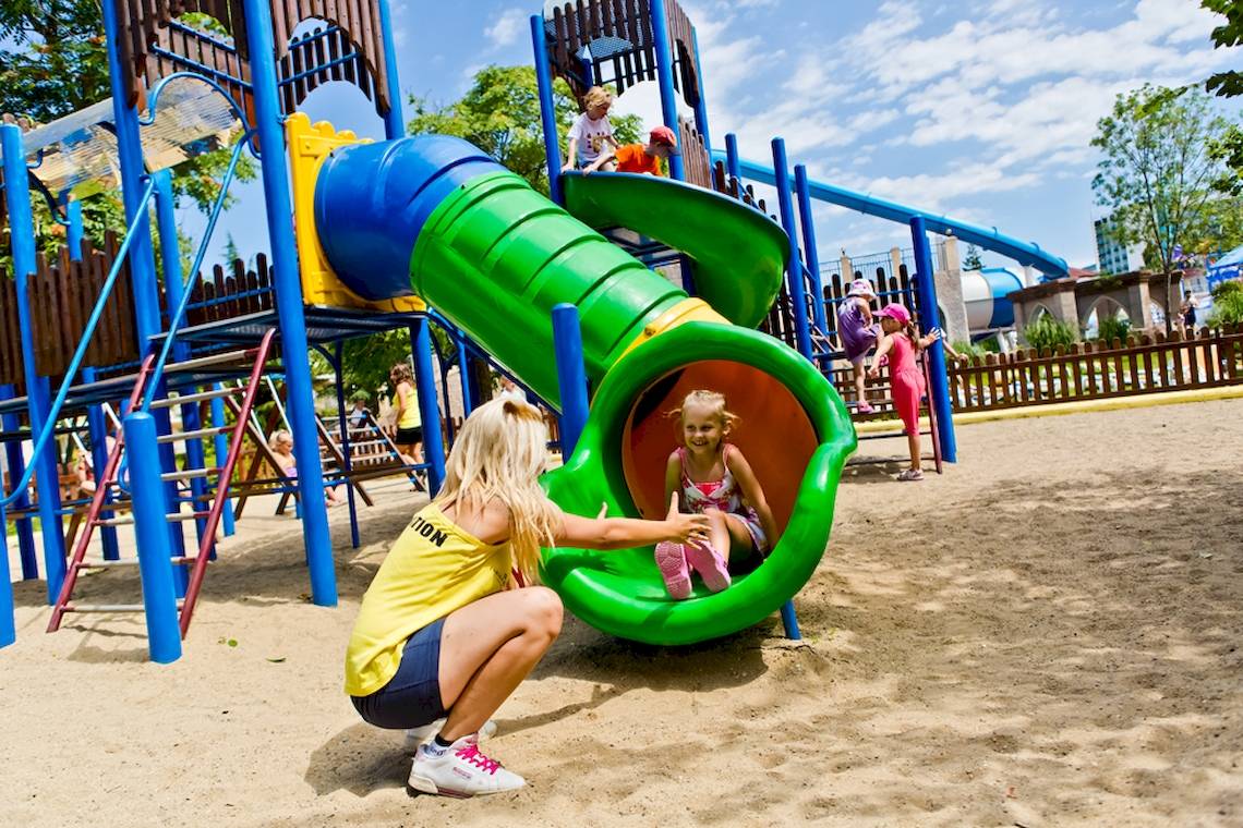 Kinder spielen im DIT Evrika Beach Club Spielplatz mit Rutschen und Klettergerüsten.