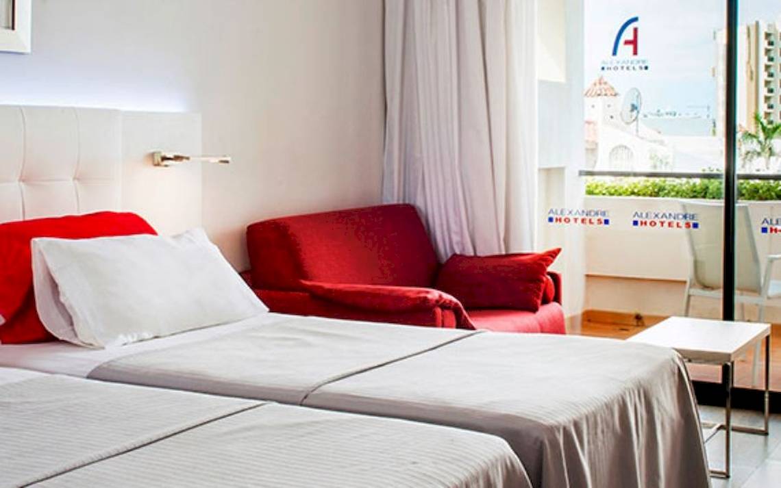 Doppelzimmer im Alexandre Hotel Gala mit zwei Betten, rotem Stuhl und Balkon.