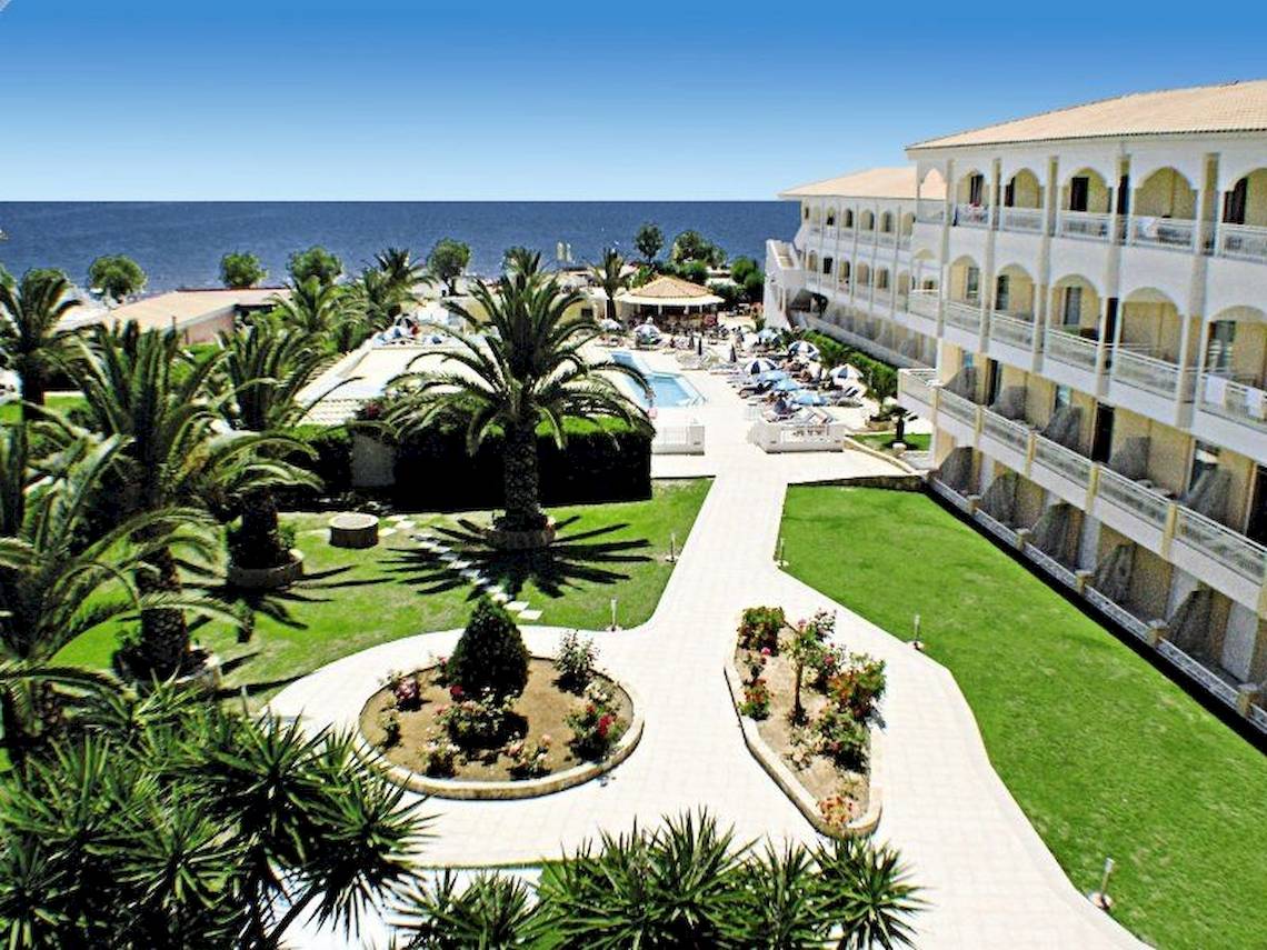 Außenansicht des Poseidon Beach Hotels mit Pool, Rasen und Meer im Hintergrund